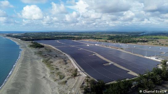 Aerial view of a coastline, sandy shore and large field of solar panels amid sparse greens